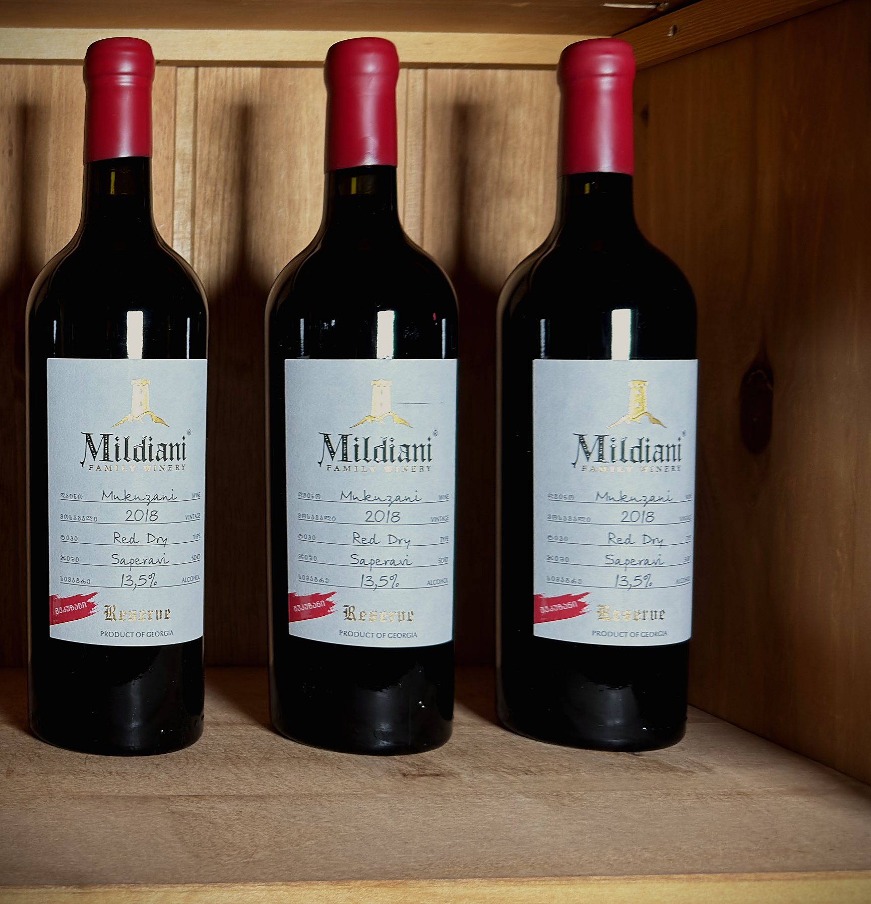 Three bottles of Mildiani Mukuzani Reserve on the wine-house shelf