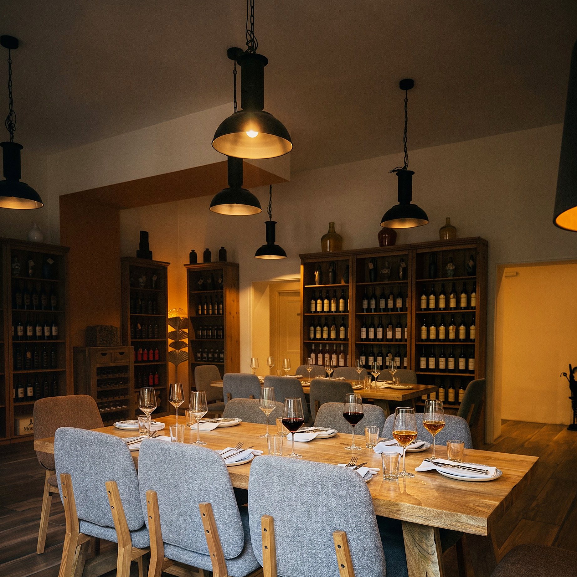 The long table laid down its full length for a party, wine poured, shelves of bottles behind